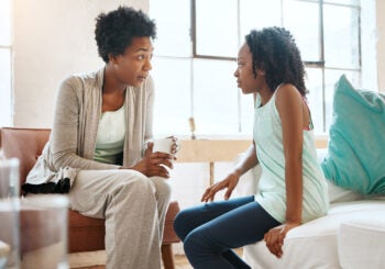 Adult and child sit facing each other in a bright living room, appearing to talk.