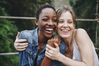 Two women smiling and embracing outdoors.