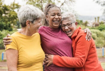 Three friends smiling and embracing outdoors.