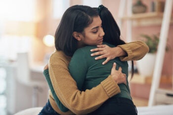 Two people embrace in a close hug indoors.
