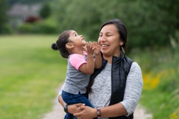 Adult holding a young child outdoors as they smile and interact.