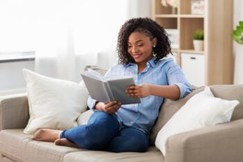 Woman sitting cross-legged on a sofa and reading a book