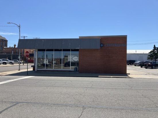 Brick Centerstone storefront with large front windows beside a stop sign.