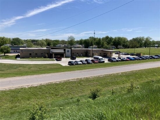Centerstone building with a parking lot beside a road and grassy slope under a blue sky.