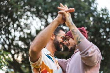 Two men standing close together outdoors with their raised hands touching overhead.