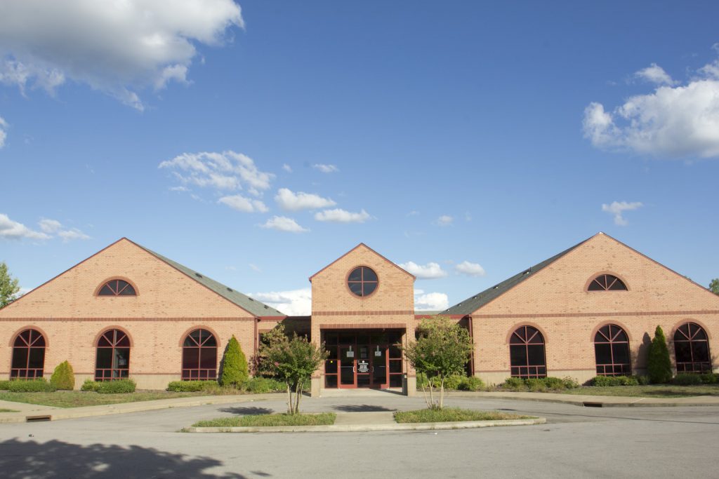 Brick building with arched windows and a central glass entrance beneath a blue sky.