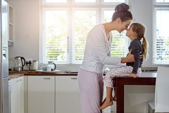 Adult holding a child seated on a kitchen counter as they touch foreheads.