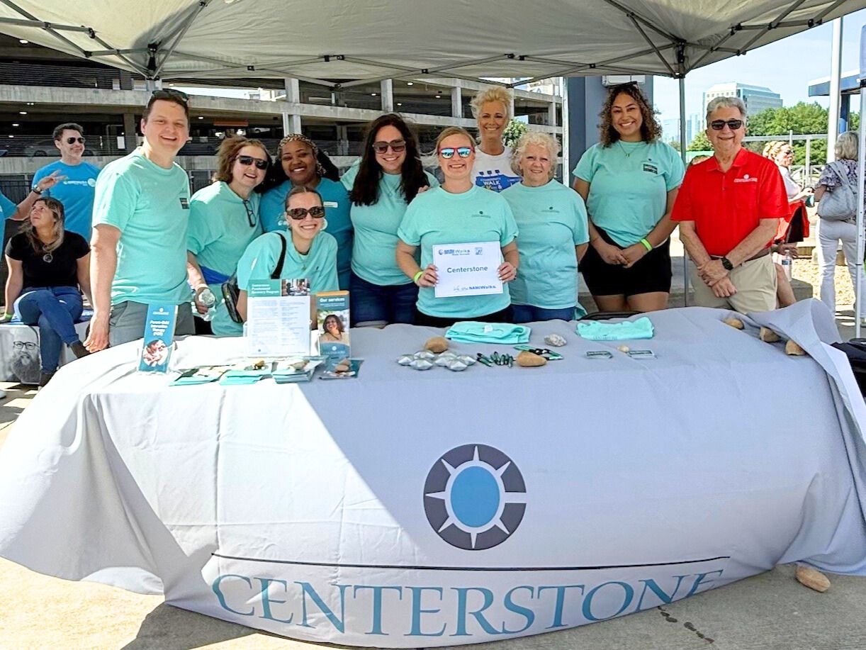 Staff at NAMI in TN Several Centerstone staff posing and smiling behind a table as they share brochures, cards, and swag at an event.