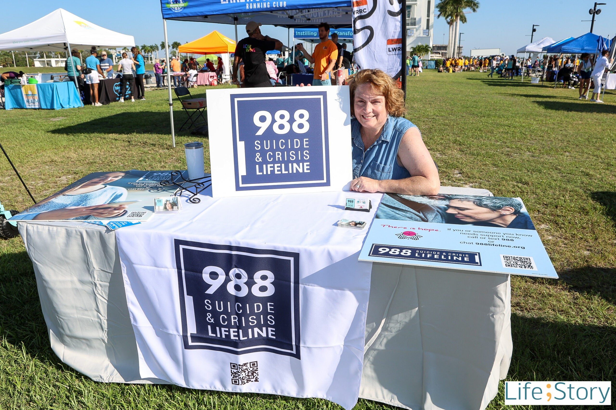 Centerstone staff at an outdoor event booth beneath a tent on a sunny day promoting 988 Crisis Services.