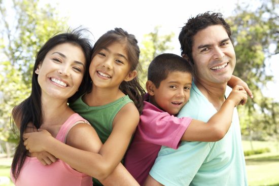 Two adults and two children smiling and hugging together outdoors.