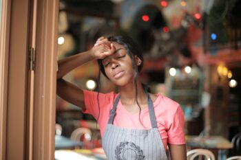 woman wearing pink shirt and gray apron leaning on brown doorway
